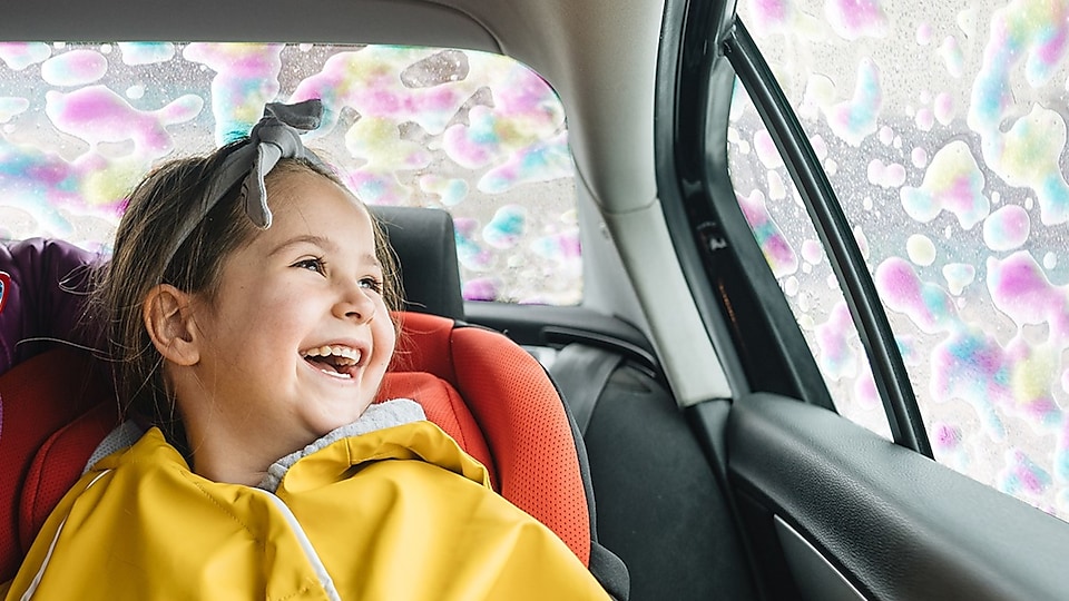 Child in car seat smiling at soapy windows inside car wash