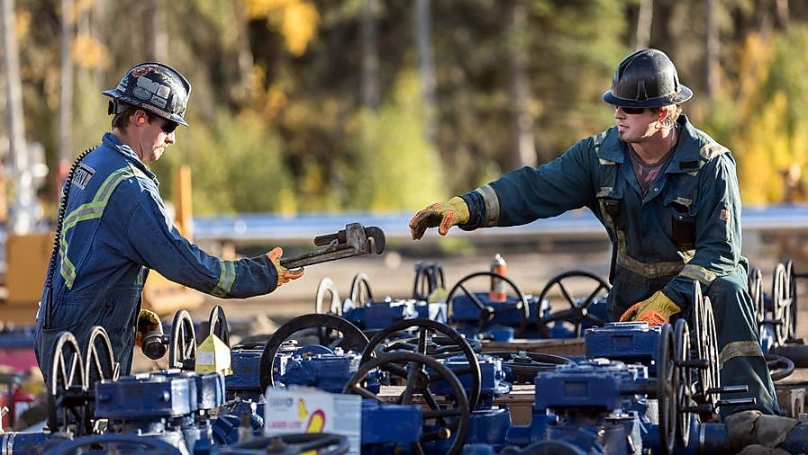 A man passes a tool to another worker at a Groundbirch well site.