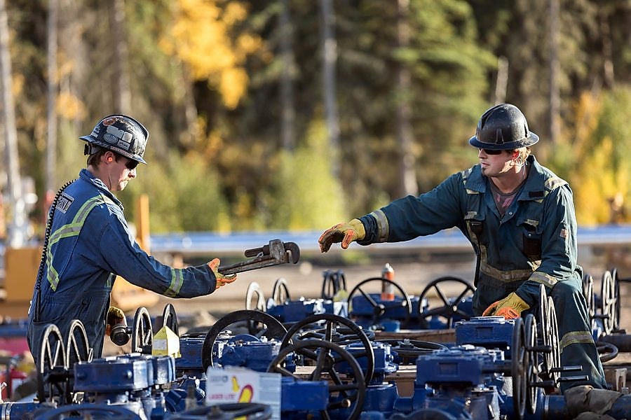 A man passes a tool to another worker at a Groundbirch well site.