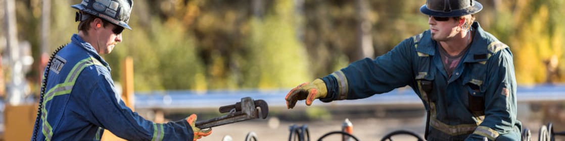 A man passes a tool to another worker at a Groundbirch well site.