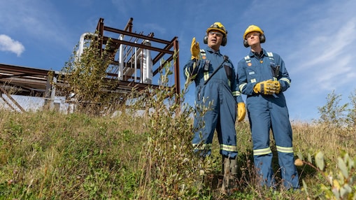 should be two male employees in grass with infrastructure behind them