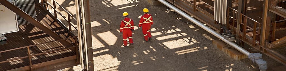 Two shell engineers in red dress walking in the factory