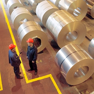 Two factory workers standing next to rolls of steel