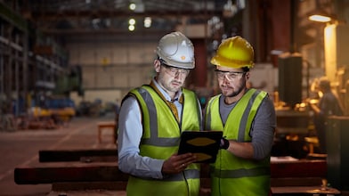 Male engineer and worker using digital tablet in dark factory
