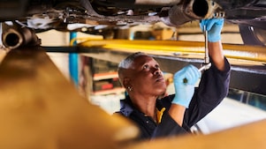 An oil-change technician in a shop working under a car and benefitting from using Shell lubricants.