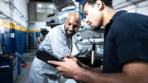 Two technicians at a service & tire shop working on a mid-size SUV to perform an oil change and check the tire pressure.