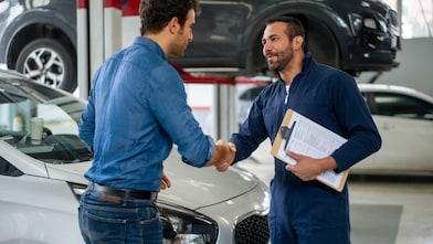 Satisfied customer shaking hands with an oil-change technician after a successful car service that encourages customer loyalty.