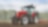  A red tractor ploughing a muddy field with trees in the background