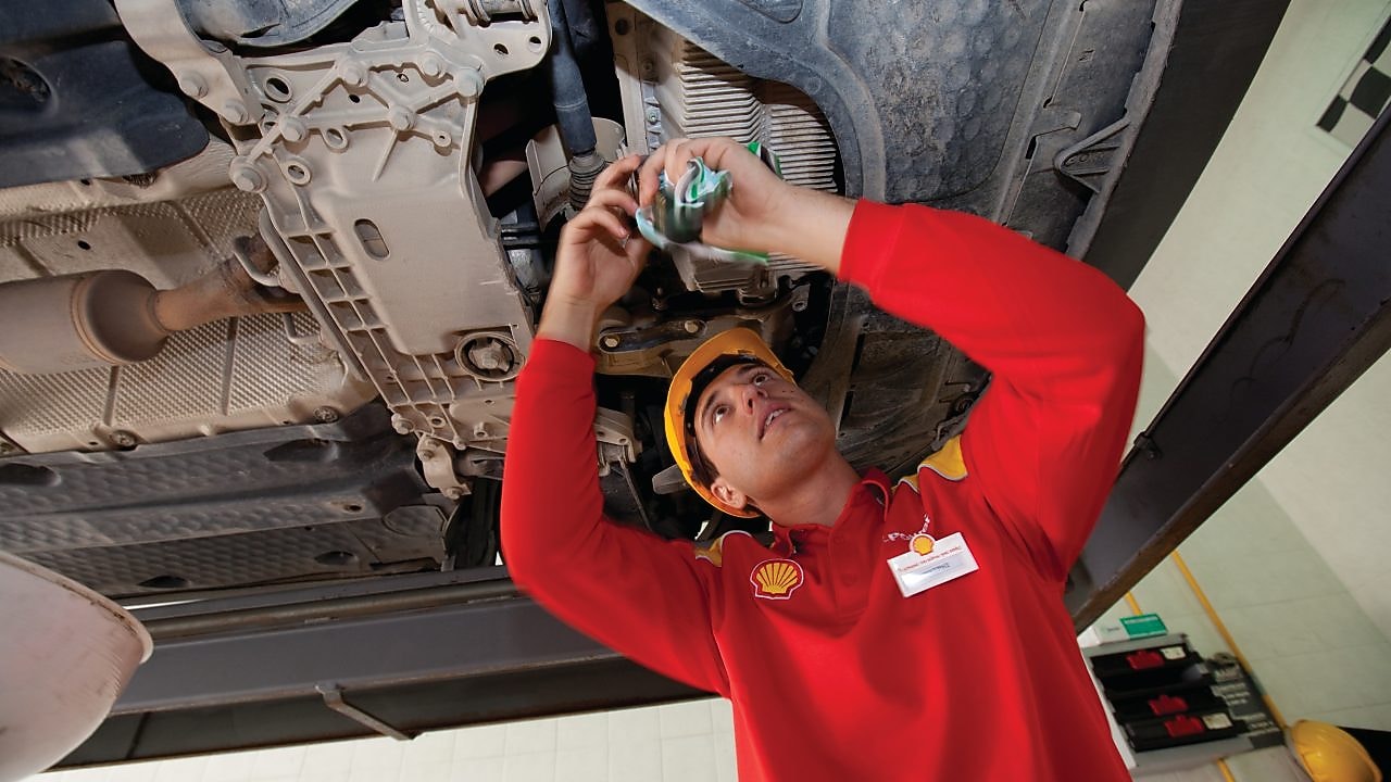two cars in a garage, one yellow and one white, with their bonnets open, and some car tyres in the background