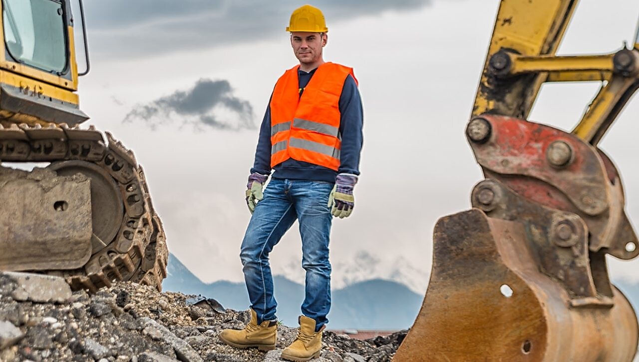 Man wearing a safety suit close to an excavator