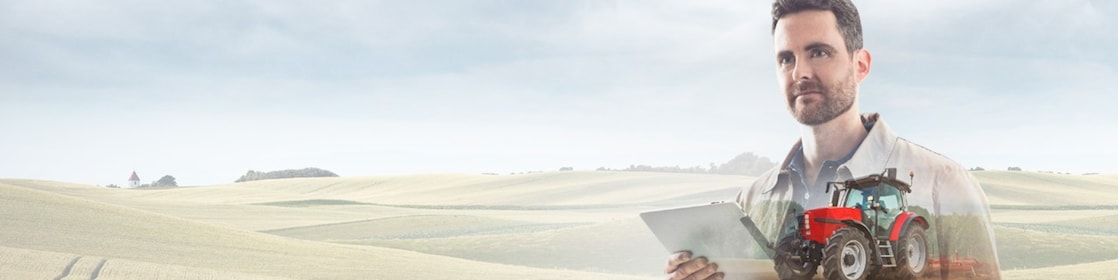 man reading a document with a background of fields and a red tractor