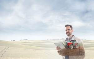 man reading a document with a background of fields and a red tractor