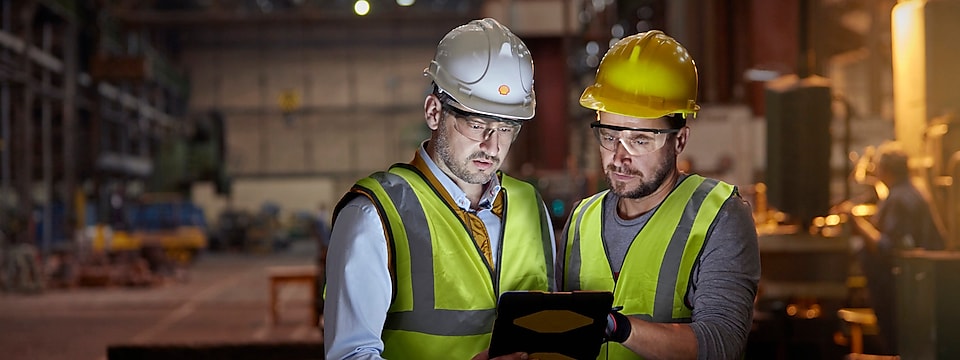 Male engineer and worker using digital tablet in dark factory