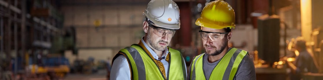 Male engineer and worker using digital tablet in dark factory