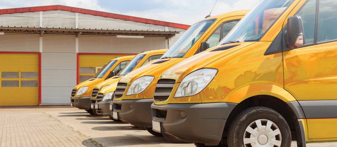 A fleet of yellow vans in front of a garage