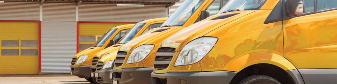 A fleet of yellow vans in front of a garage