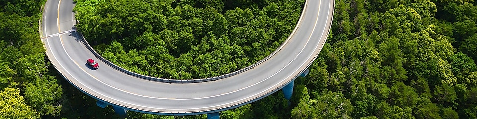 Overhead shot of a car on a winding road surrounded by trees