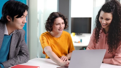 Three individuals engaging in a collaborative discussion around a laptop in a modern office setting.