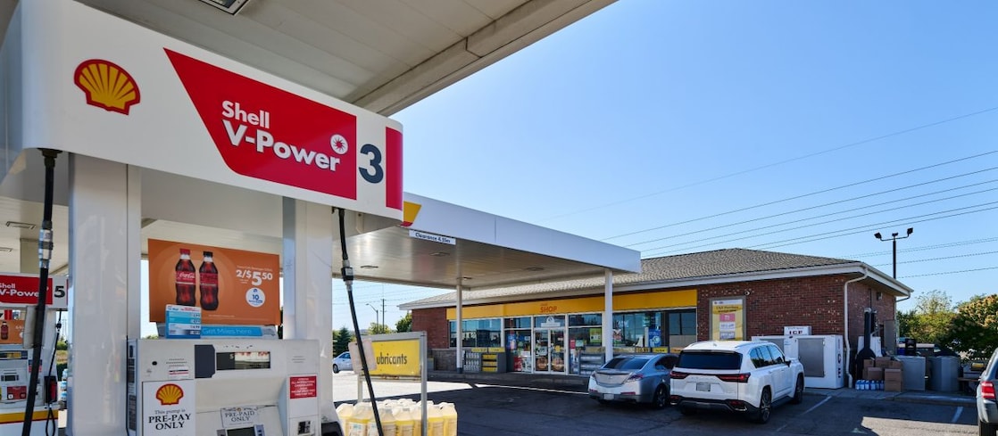 Shell service station canopy with illuminated Shell logo and fuel signs at dusk.