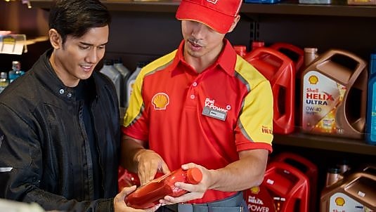 Shell service station employee assisting a customer by explaining a motor oil product.