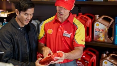 Shell service station employee assisting a customer by explaining a motor oil product.
