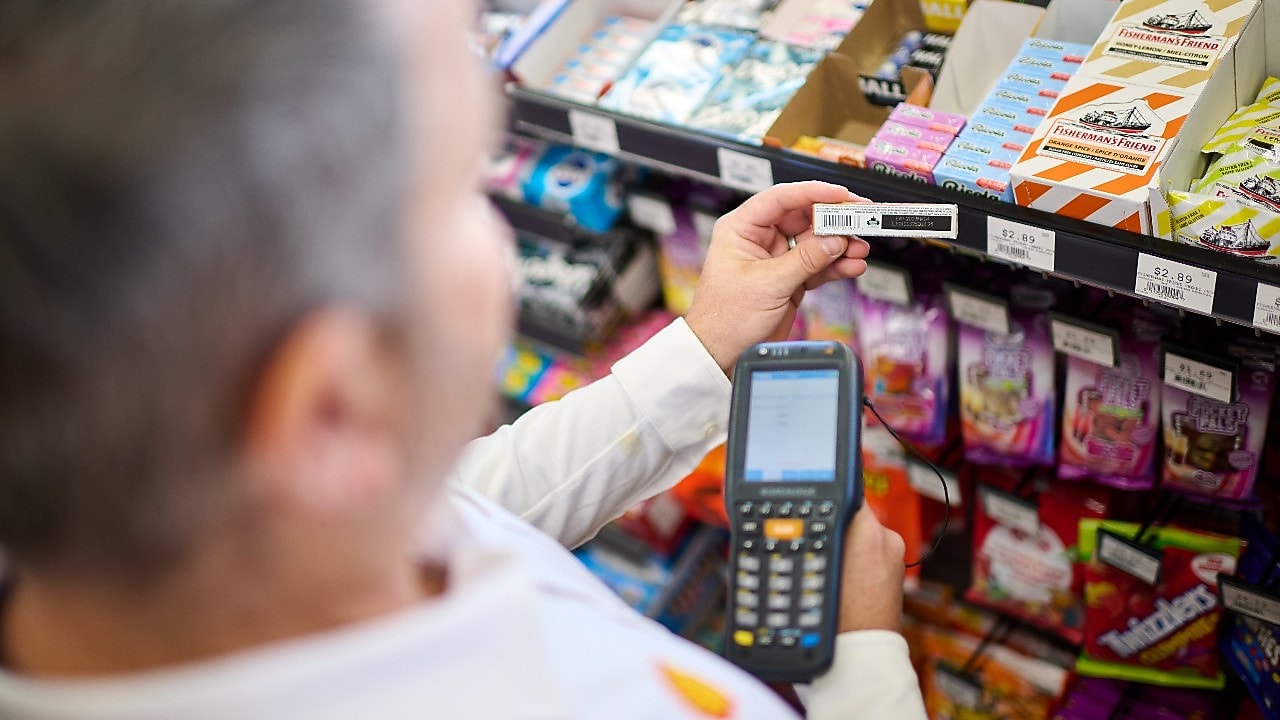 Customers using a mobile phone to make a digital payment at a Shell service station store.