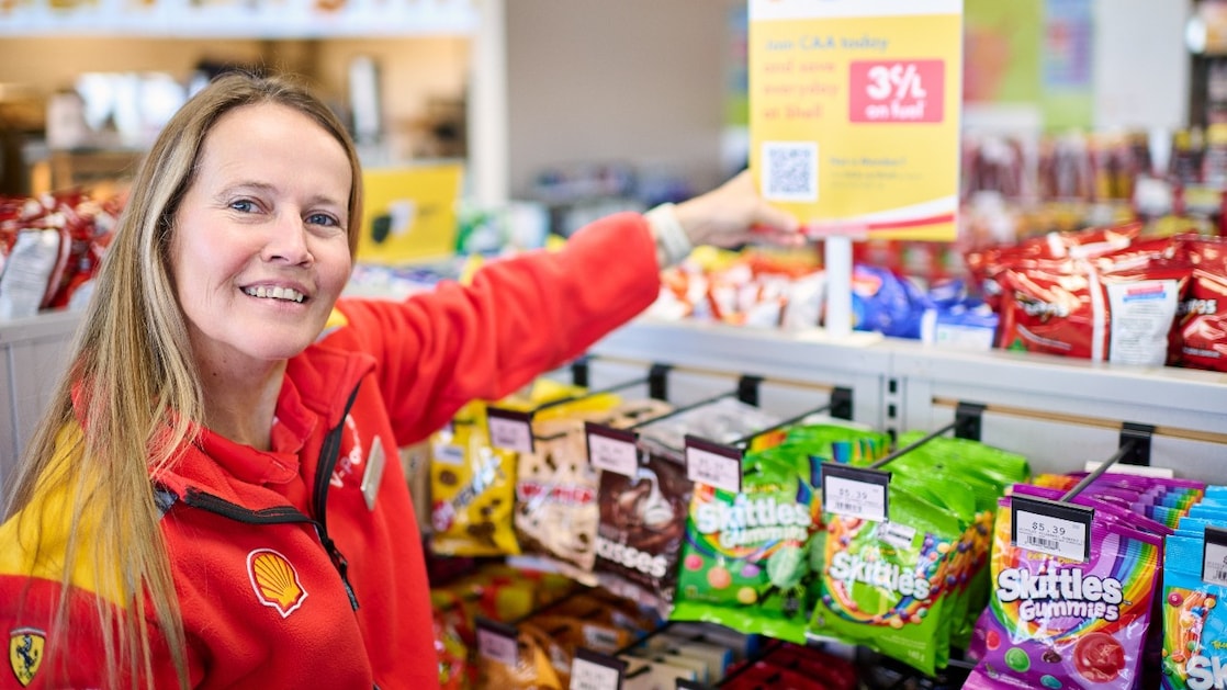 Two Shell service station employees walking together on the forecourt in front of Shell V-Power fuel pumps.