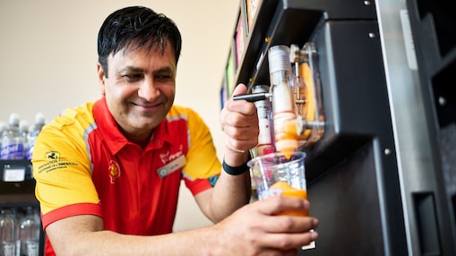 Father and daughter ordering food at a Shell Café counter served by a smiling employee.