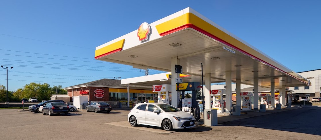 Illuminated Shell service station forecourt at night with fuel pumps for Shell V-Power, AutoGas, and AdBlue, against a dark sky backdrop.