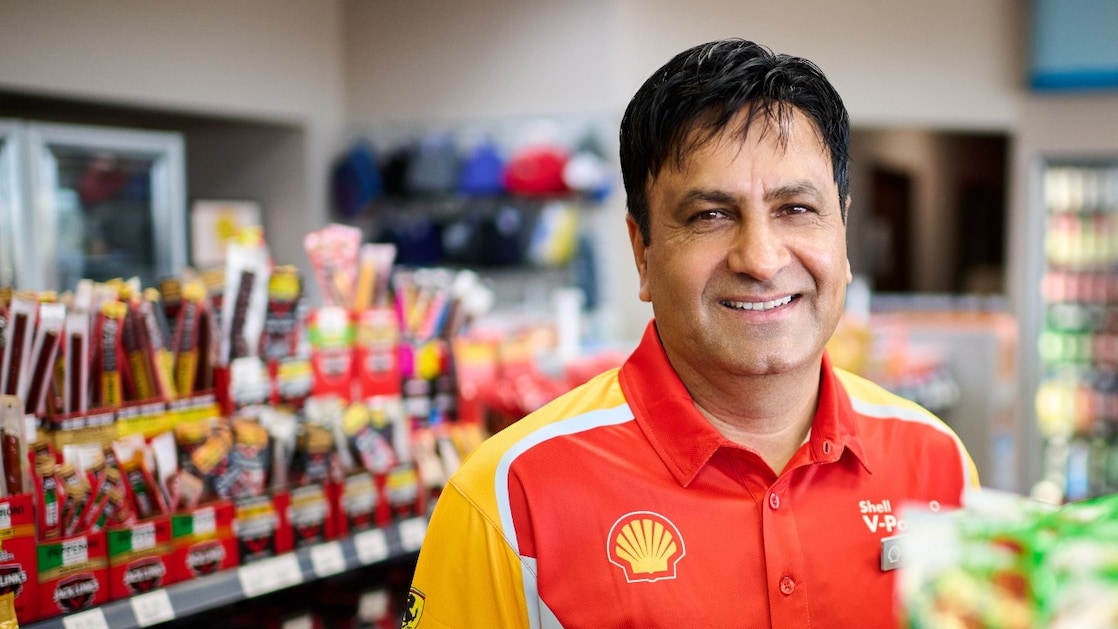 Shell service station employee in uniform standing confidently with arms crossed in front of a Shell station.