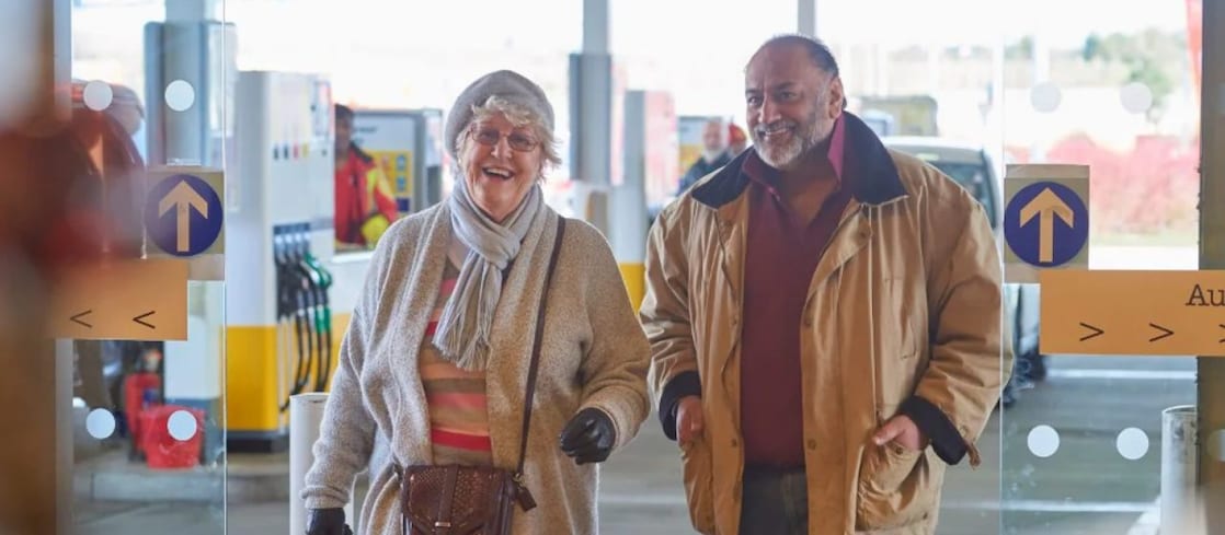 Two older customers smiling as they walk into a Shell service station store.