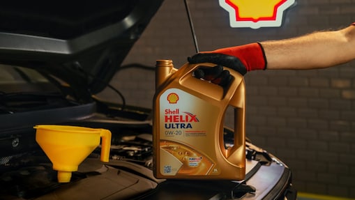 Close-up of a mechanic holding a container of Shell Helix Ultra motor oil with a funnel placed in a car engine.