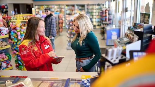 Smiling customer in a car making a contactless payment with a credit card to a Shell service attendant.