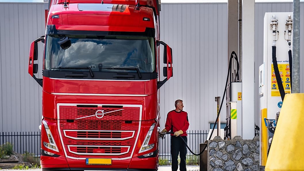Truck driver refueling a large red Volvo truck at a Shell station fuel pump.
