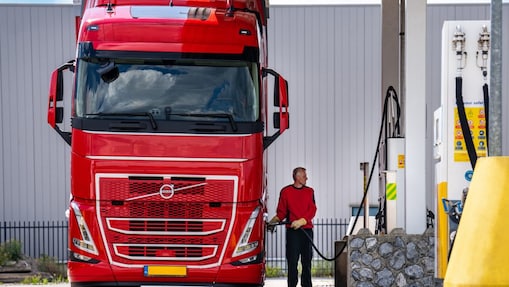Truck driver refueling a large red Volvo truck at a Shell station fuel pump.
