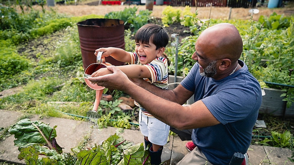 Un homme aidant un enfant souriant à arroser les plantes d’un jardin