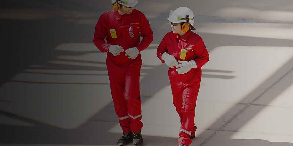 Un travailleur et une travailleuse portant une combinaison rouge, un casque blanc et un protecteur auditif en train de marcher