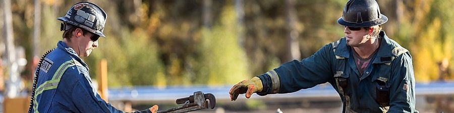 A man passes a tool to another worker at a Groundbirch well site.