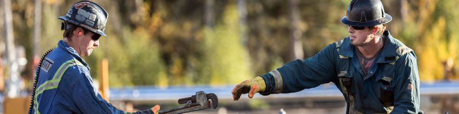 Un homme donne un outil à un autre travailleur à un chantier de puits de Groundbirch.