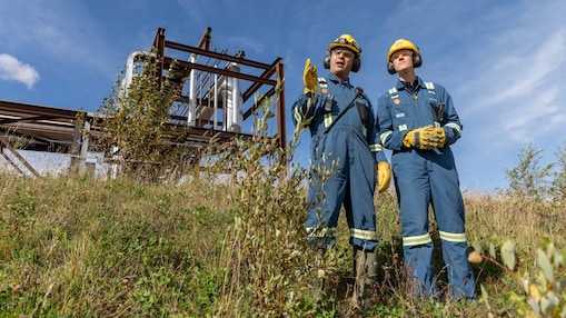 should be two male employees in grass with infrastructure behind them