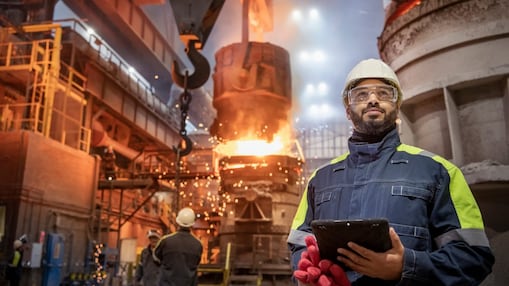 a man in PPE with iPad and steel making process in the background
