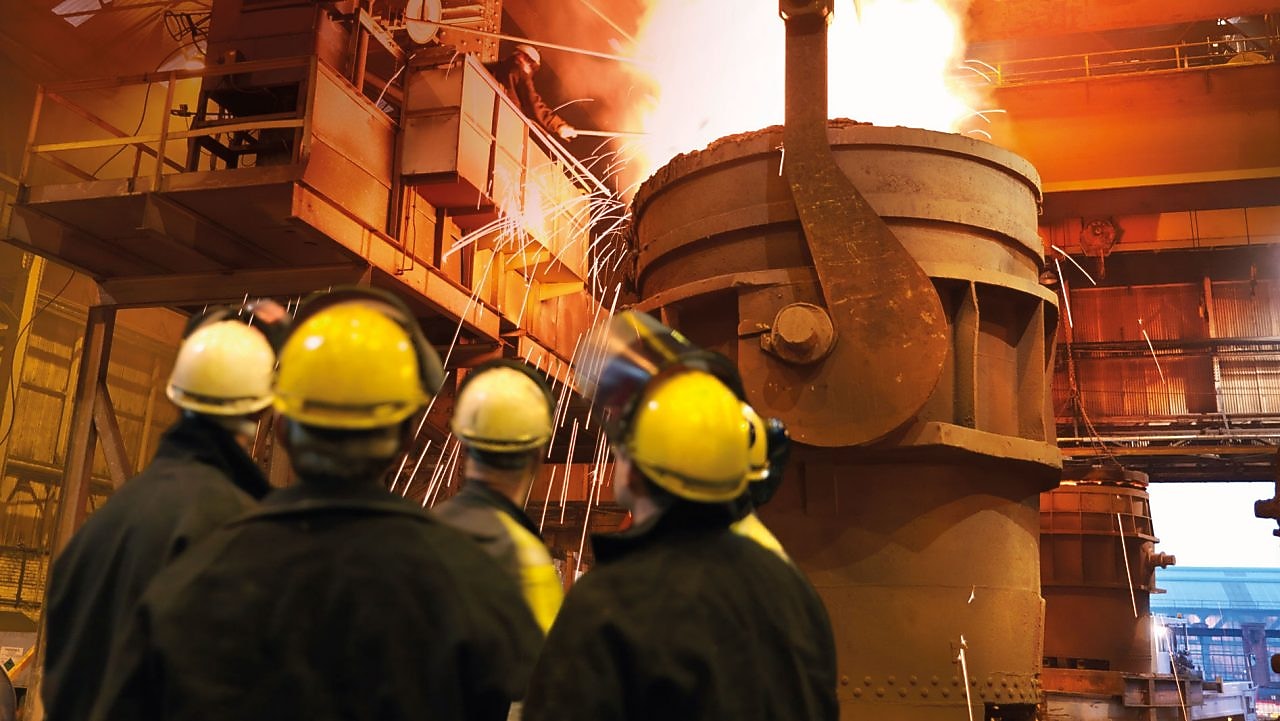 Workers watching heavy machinery in a metal processing plant