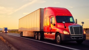 Two commercial transport semi-trucks driving on a remote highway.