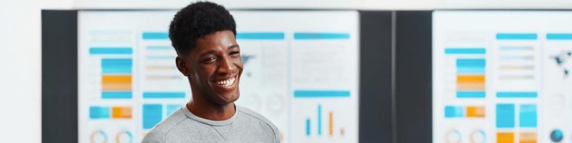 Professional presenting data on a tablet in a modern workspace, with large digital dashboards and charts displayed on screens behind them.