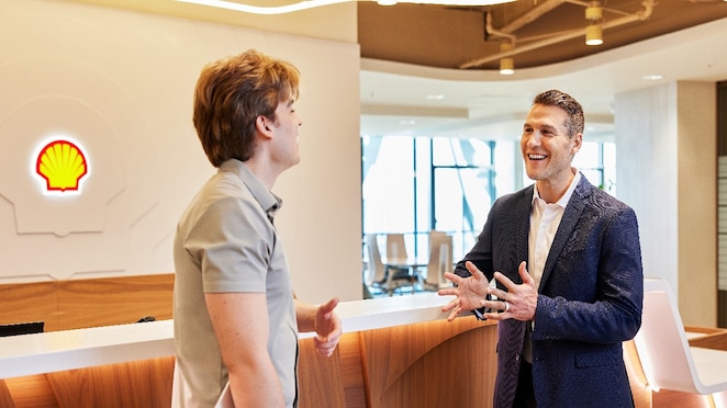 Two male colleagues collaborating in a corporate office environment, with Shell branding visible behind them.