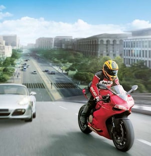 Moto rouge et conducteur sur une route avec des voitures et des bâtiments dans l&rsquo;arrière-plan.