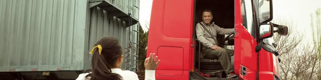 Homme dans une cabine de camion rouge avec porte ouverte saluant sa fille
